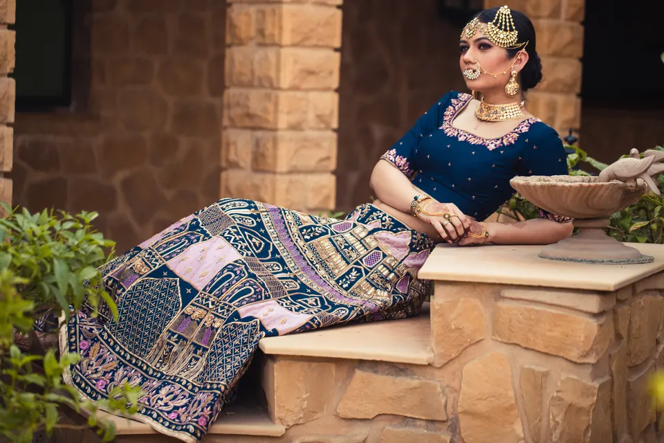 A bride reclining on a sandstone step in a navy patchwork lehenga, in a Jaisalmer courtyard